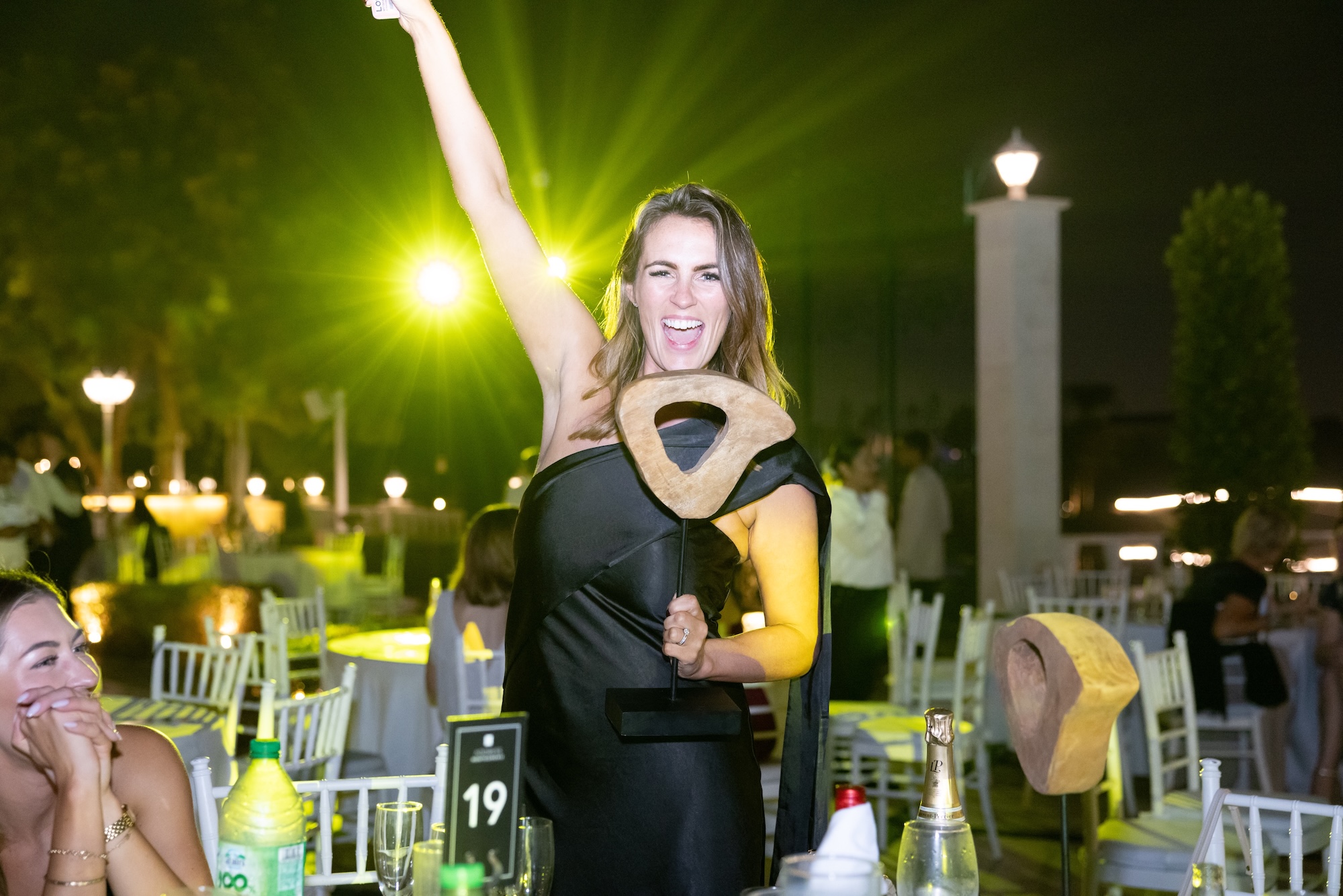 A winner celebrating with her trophy, smiling with her arm raised against golden lights at the mentl awards 2025